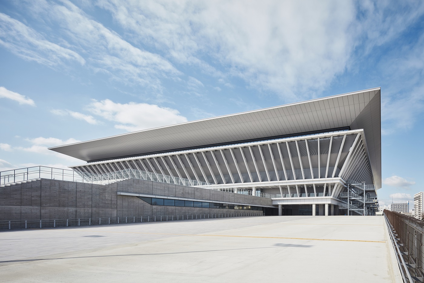 Contemporary multi-tiered building with a large slanted roof and diagonal white supports against a blue sky.