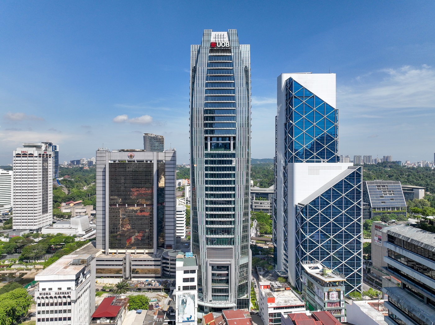 A city skyline of tall glass office towers, with a central skyscraper bearing the UOB logo against a clear blue sky.