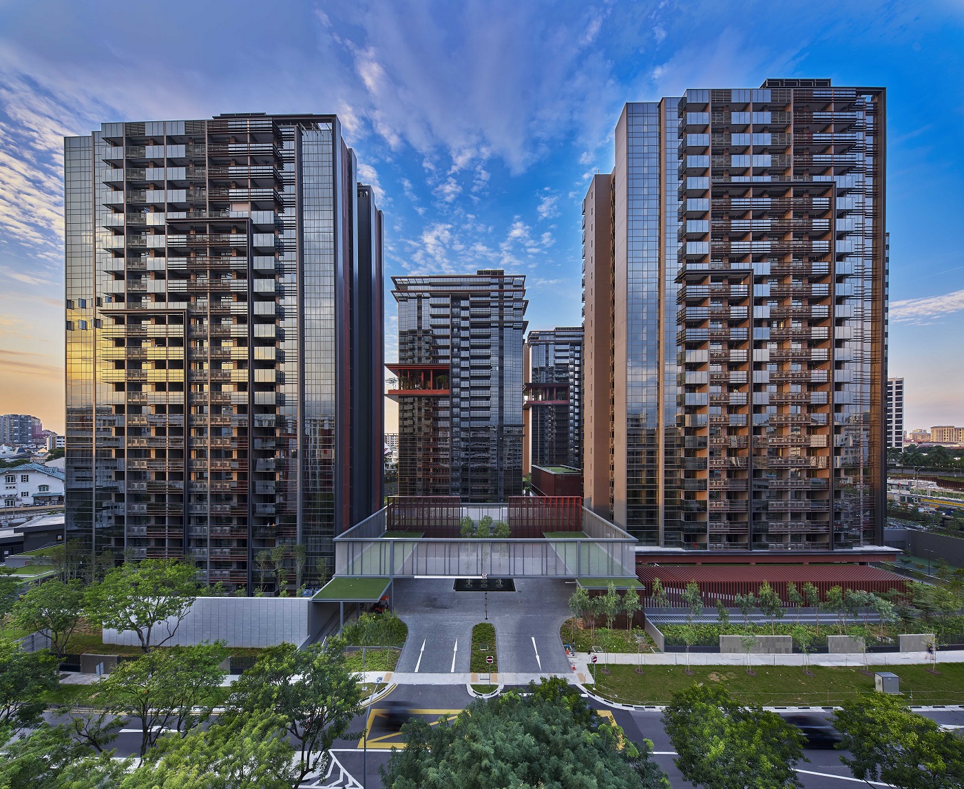Modern glass residential towers forming a clustered development, with a central courtyard and green landscaping below against a blue sky.