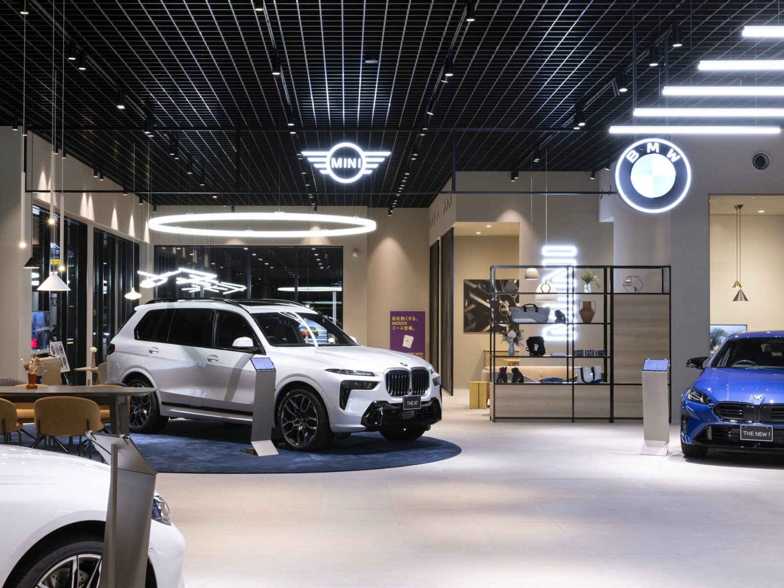 Modern car showroom featuring a white SUV on display under bright ceiling lights and illuminated MINI and BMW logos.