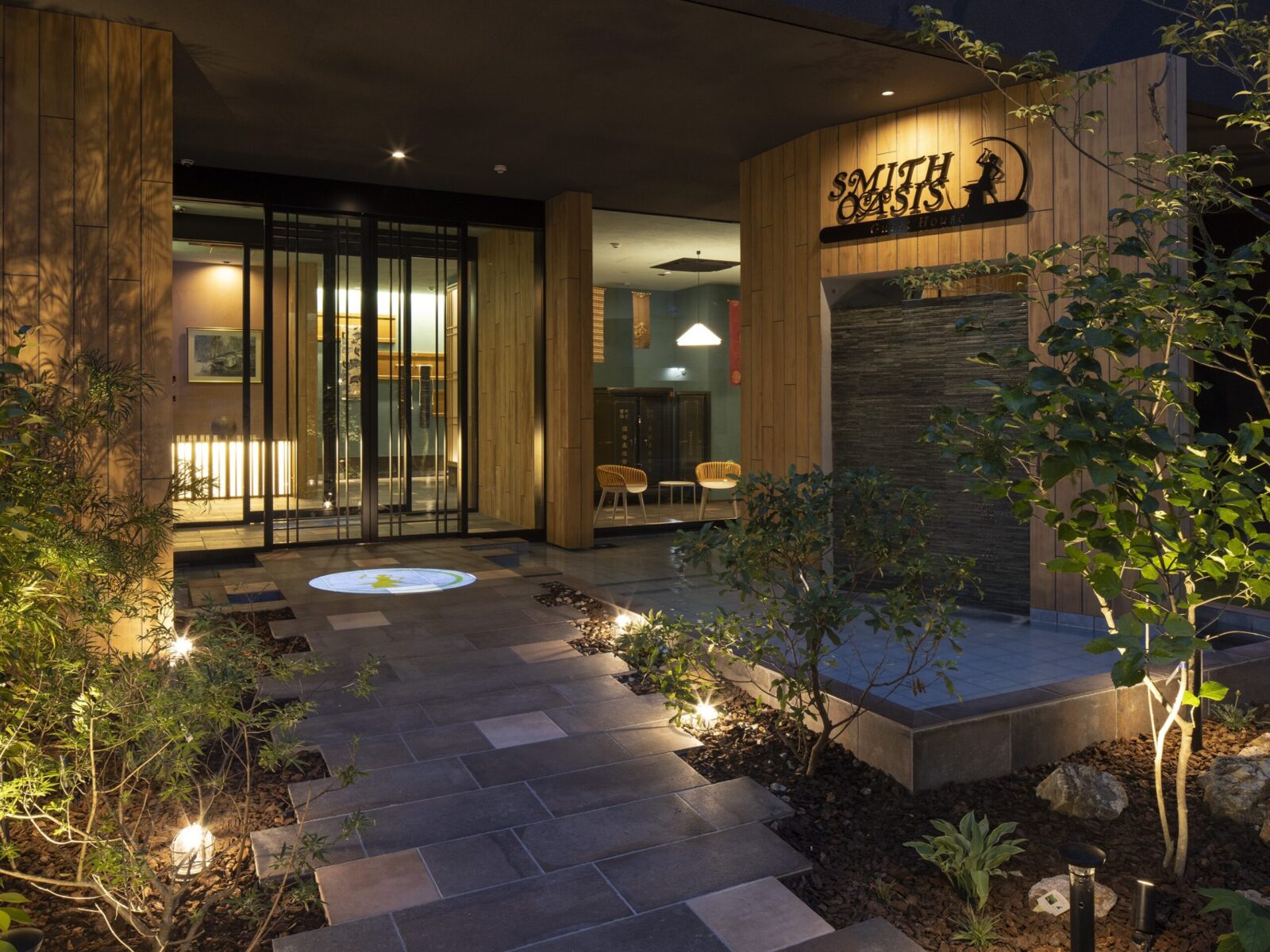 Night exterior of the Smith Oasis Club House with wooden panels, glass doors, and warm outdoor lighting.