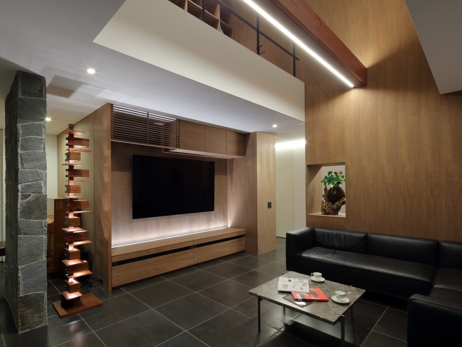 Modern living room with wood-paneled walls, built-in TV wall, and black leather sofa on a dark tile floor