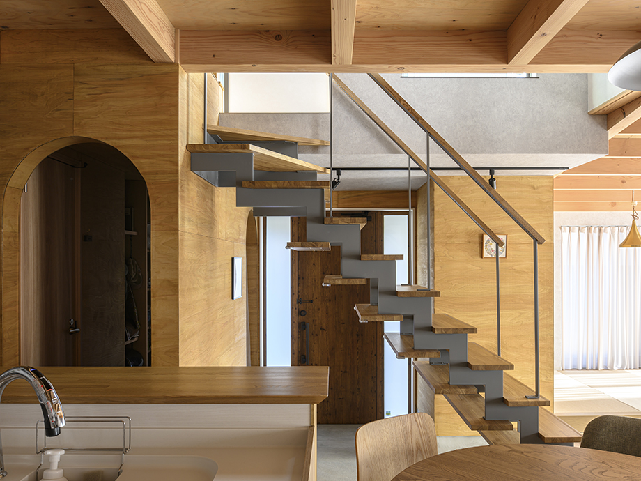 Contemporary home interior with a zigzag wooden staircase and metal supports, open living space, and exposed wooden beams.