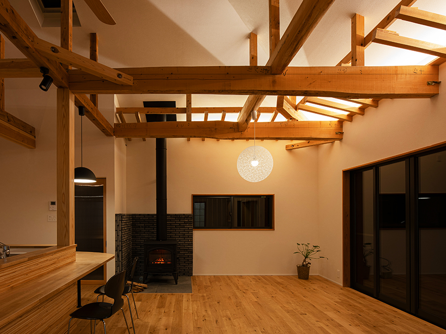 Open living space with exposed timber beams, a wood-burning stove, and a round pendant light central to a warm, modern interior.