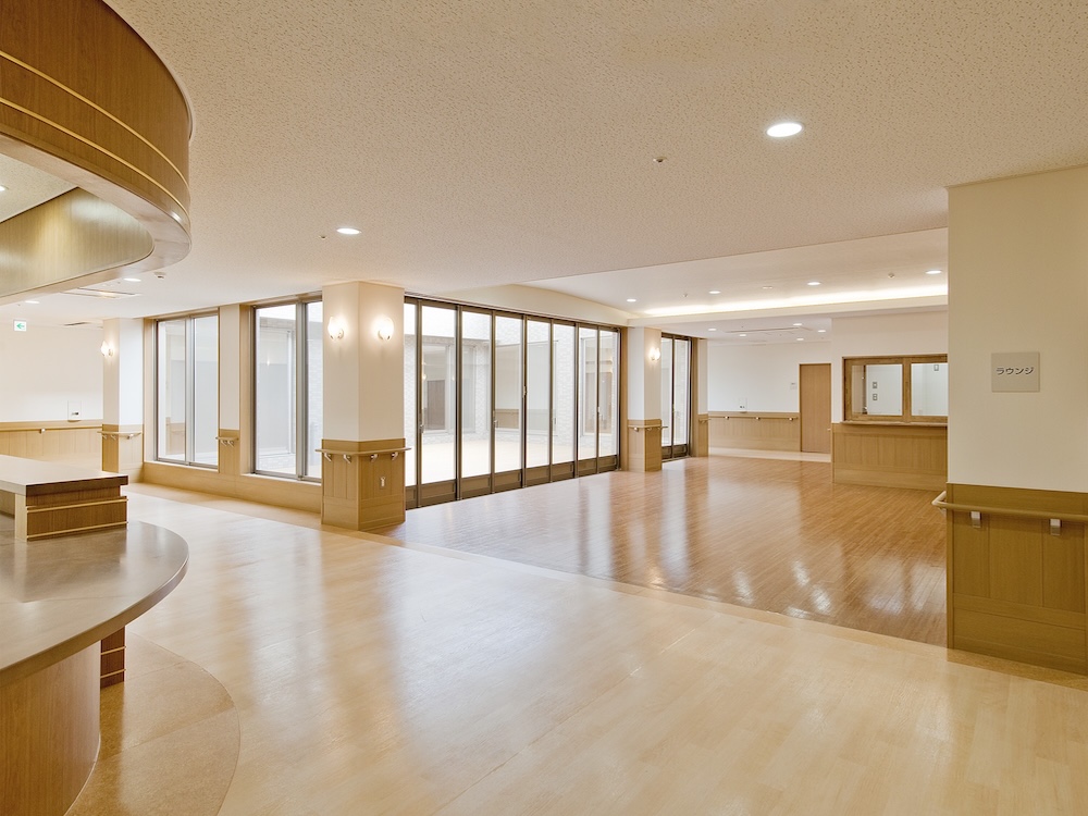 Spacious, well-lit lobby with wooden floors, glass partition walls, and a reception desk on the right.