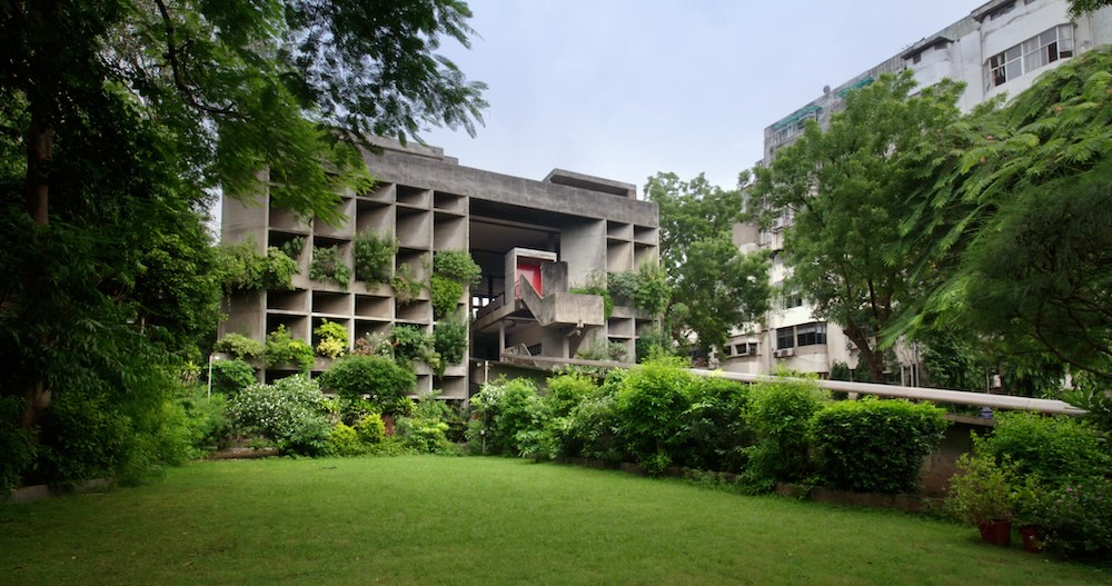 Concrete modernist building with a grid facade, framed by trees and a well-kept lawn in the foreground.