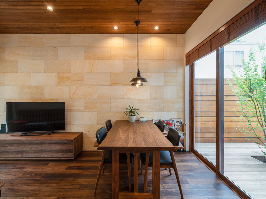 Wooden dining table with black chairs in a modern room, stone wall, TV on a wooden credenza, and large glass doors to an outdoor deck.