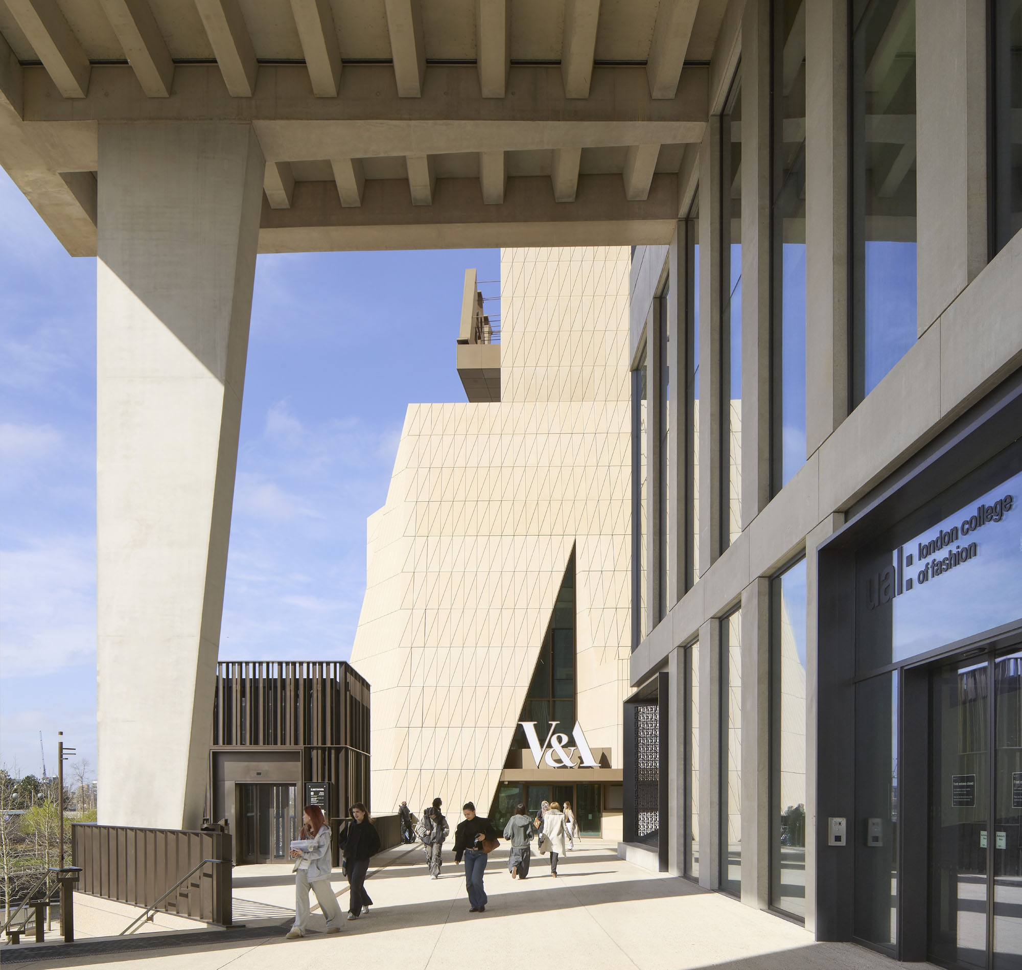 Group of people walking in a modern concrete building courtyard with large glass windows and overhead beams.
