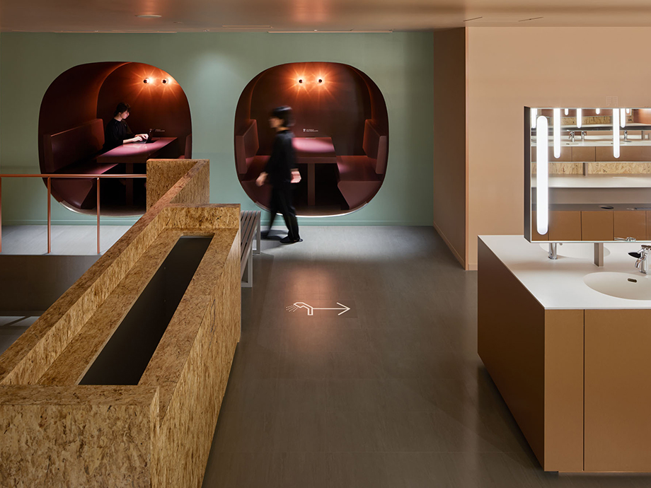 Modern interior with two red bubble seating pods along a teal wall; a person walks by as a sink area is on the right.