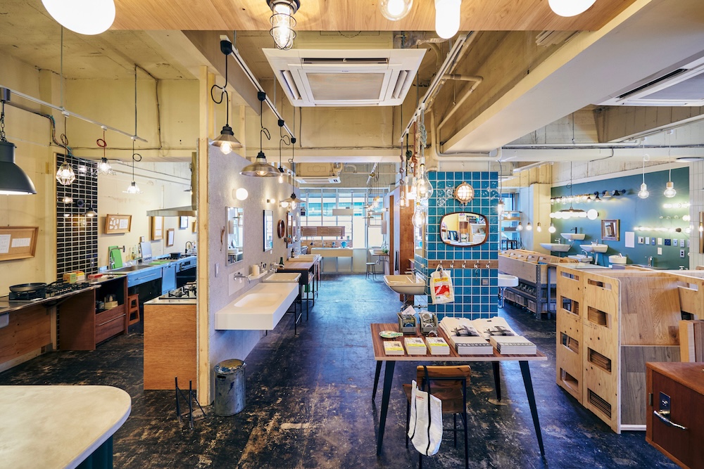 Industrial-style showroom/workspace with kitchen sinks, tables, and display shelves under warm hanging lights.